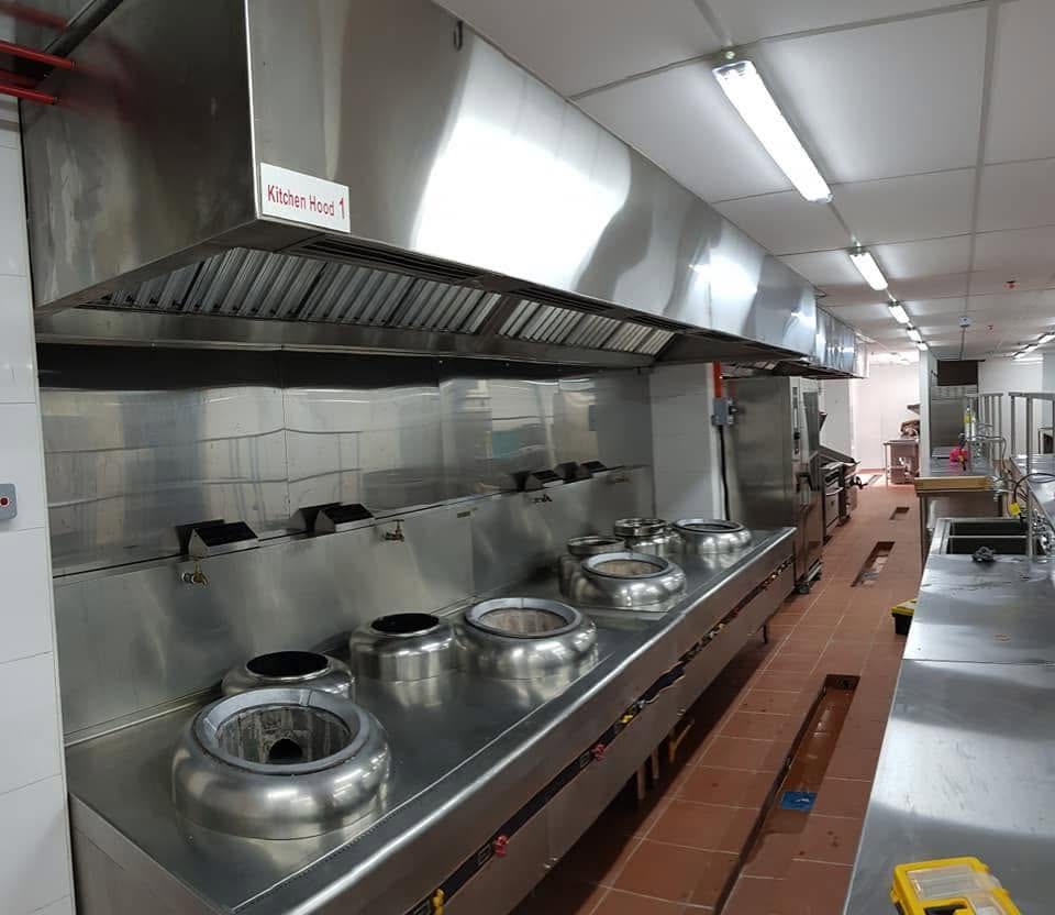 A stainless extraction hood installed over a multi-well gas wok range in a commercial kitchen.